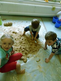 Drei Kinder spielen und formen mit Sand auf dem Boden. 