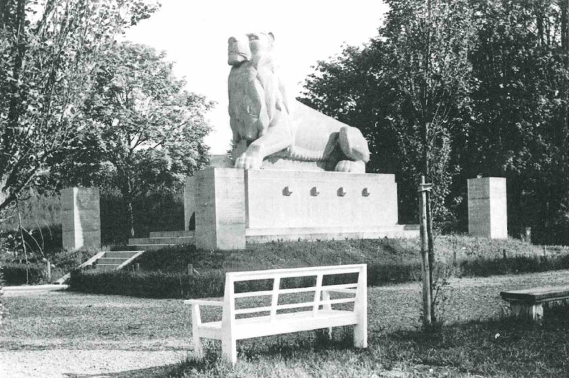 Großer Löwe auf einem Betonsockel in einem Park mit Sitzbänken 