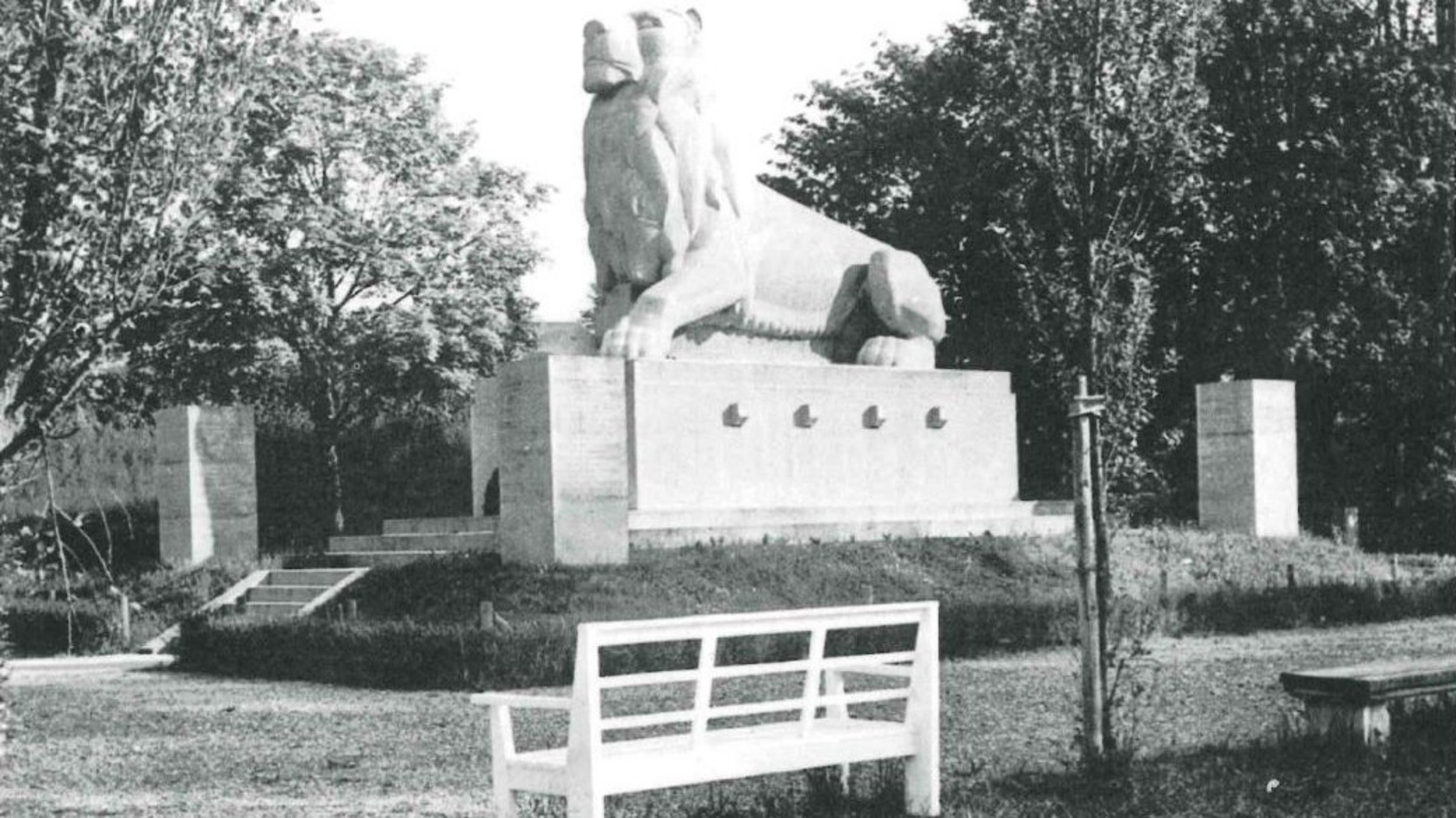 Großer Löwe auf einem Betonsockel in einem Park mit Sitzbänken