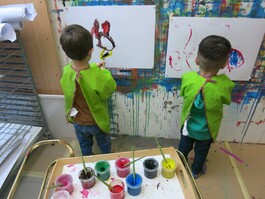 Zwei Kinder malen auf Papier an einer Wand