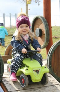 Foto aus der Kinderkrippe: Kleines Mädchen im Freien auf einem Rutschauto