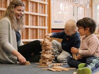 Zwei Kinder und eine Erzieherin bauen aus Holzklötzen einen Turm