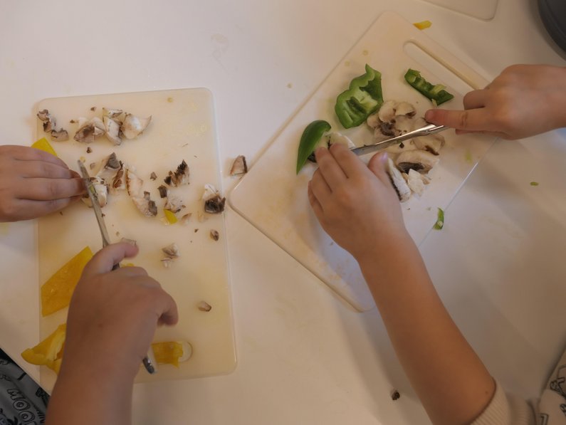 zwei Kinder beim Kleinschneiden von Gemüse, sichtbar sind nur die Hände, Messer und Schneidebrett sowie Gemüse