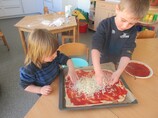 Zwei Kinder bereiten eine Pizza zu. 