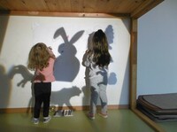 Zwei Mädchen malen Schattenfiguren an einer Wand nach.