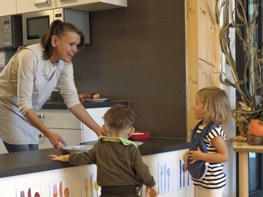 Erzieherin gibt Essen an Kinder aus.