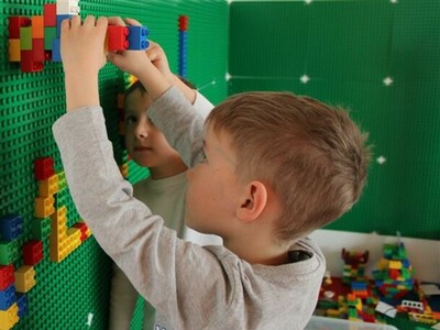 Foto aus dem Kindergarten: Ein Junge steht an einer Wand mit grünen Bauplatten von Lego und setzt Legosteine darauf