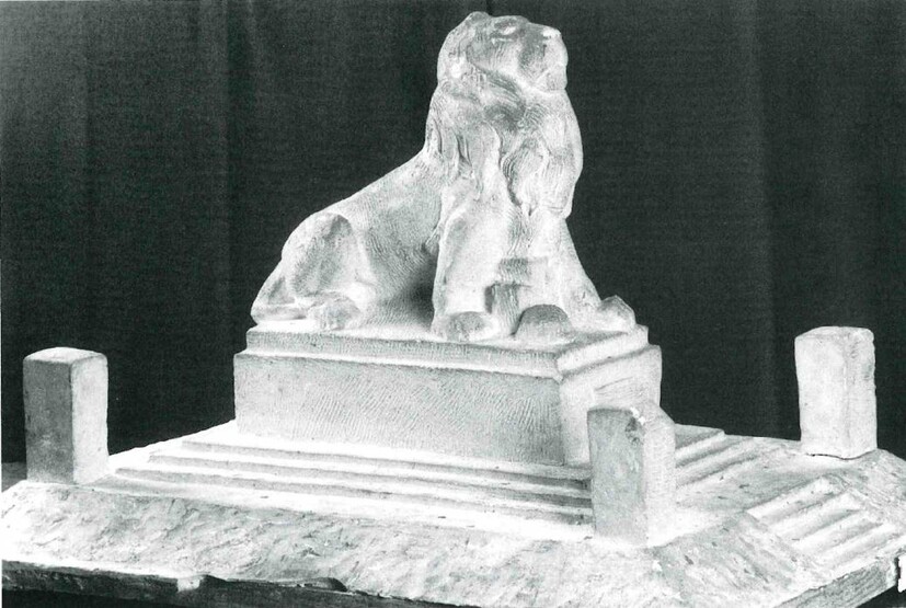Modell eines Löwen der sich auf die Vorderpfoten stützt auf einem Betonsockel