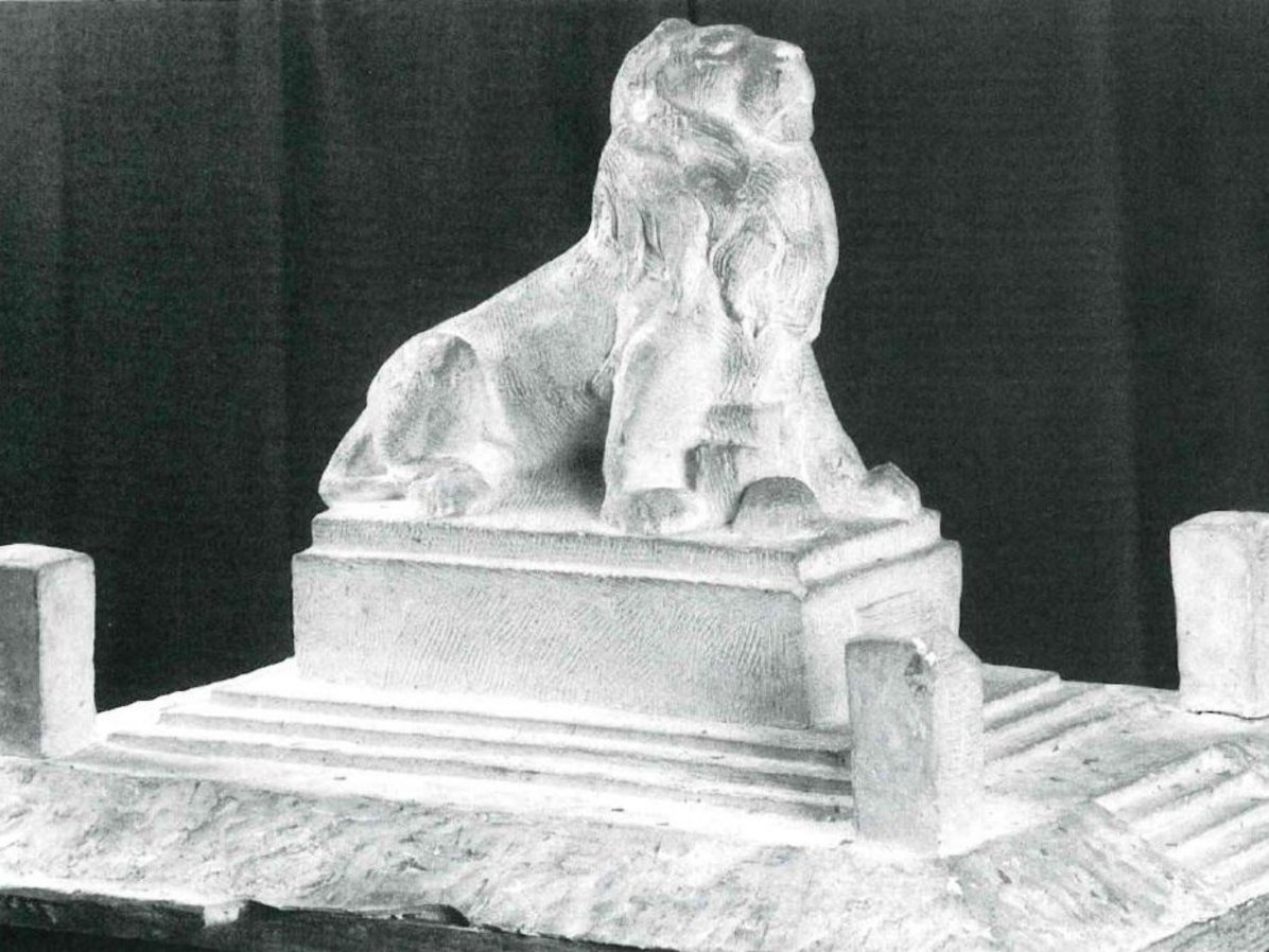 Modell eines Löwen der sich auf die Vorderpfoten stützt auf einem Betonsockel