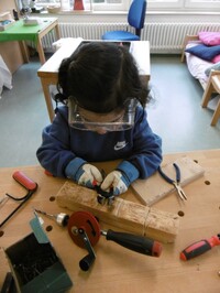 Mödchen mit Schutzbrille arbeitet an einem Stück Holz